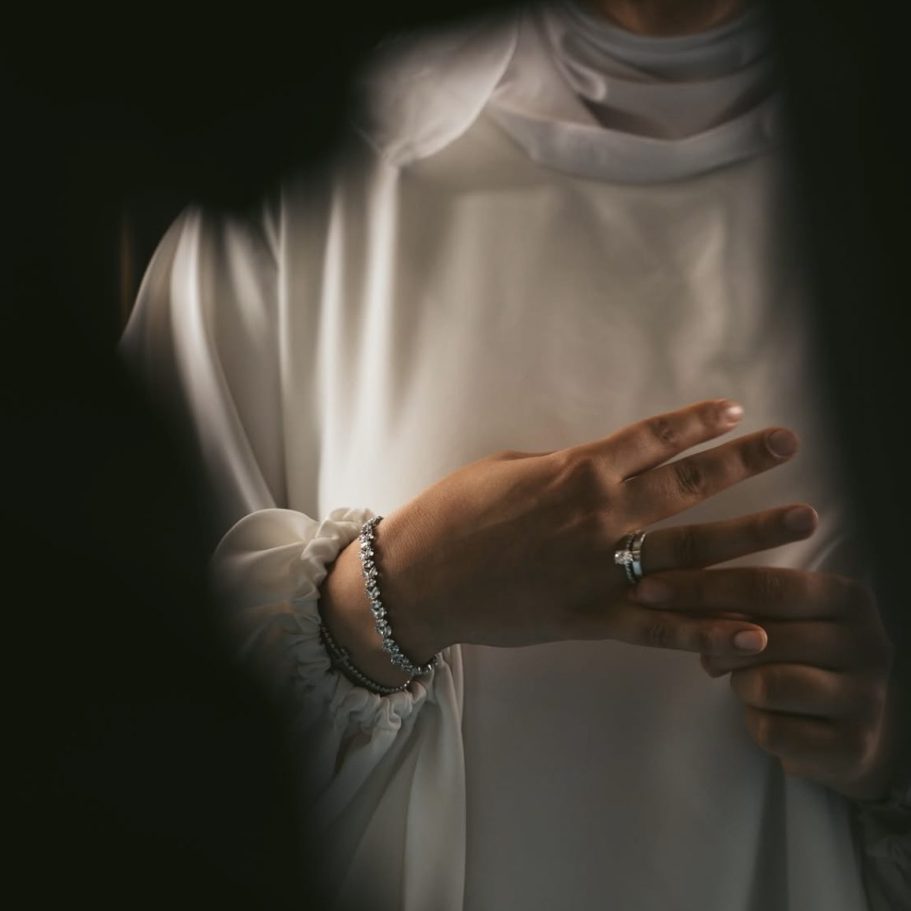 Oberkörper einer Person in weißem, fließendem Gewand, Hände mit Ringen und Armband